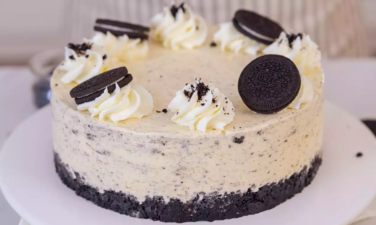Sladoledna torta z vanilijevo kremo in drobnimi črnimi koščki, na temni Oreo podlagi, okrašena s smetanovimi kapicami in celimi Oreo piškoti
