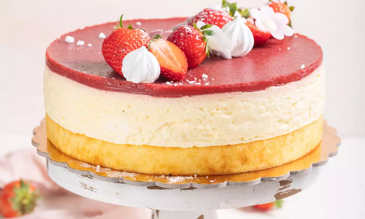 Torta z nežno rumeno kremo na zlato rjavi podlagi, pokrita z gladko rdečo plastjo, okrašena s jagodami, belimi meringami in sladkorjem